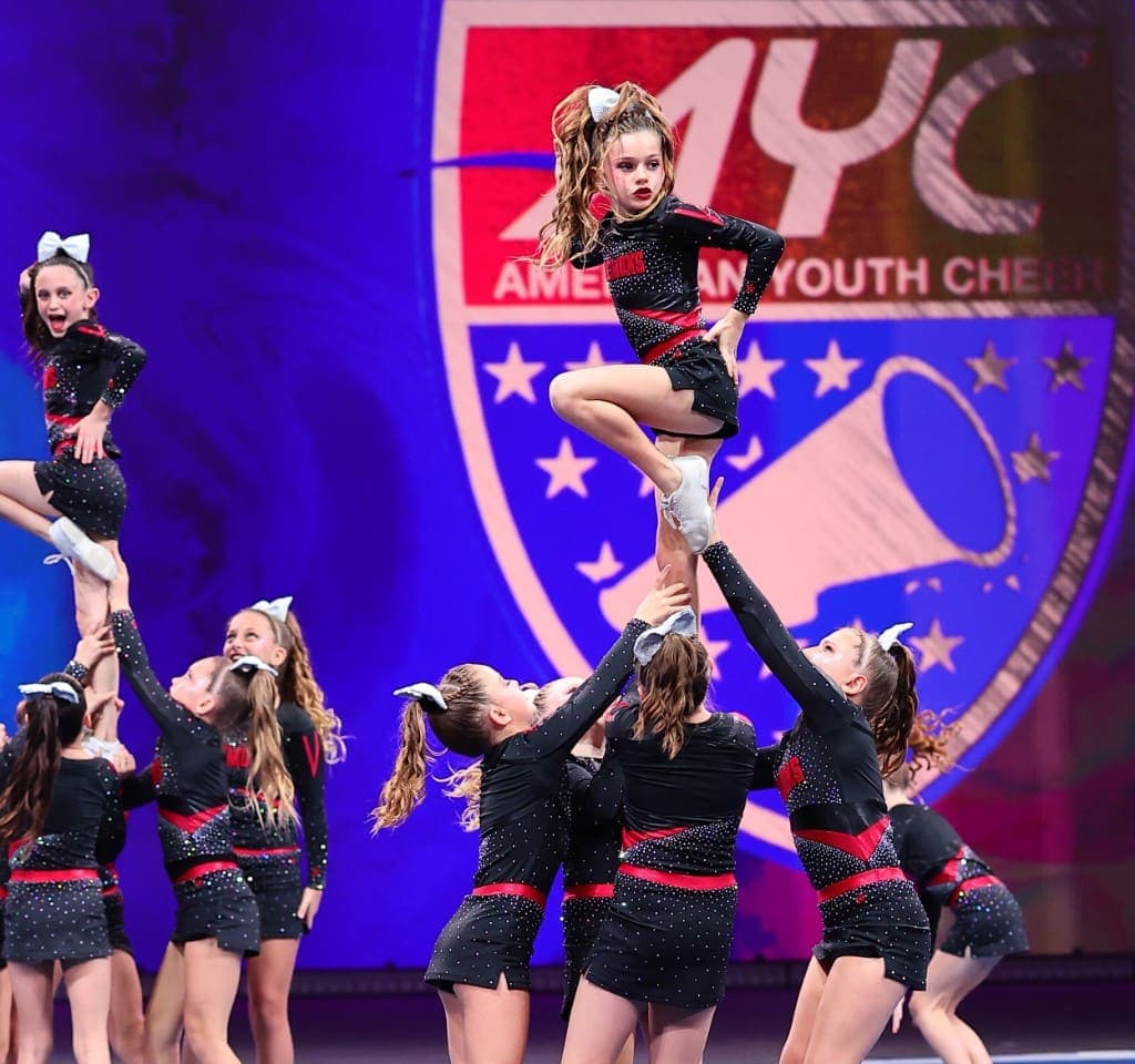 A cheer team holding a flyer in a stunt on stage