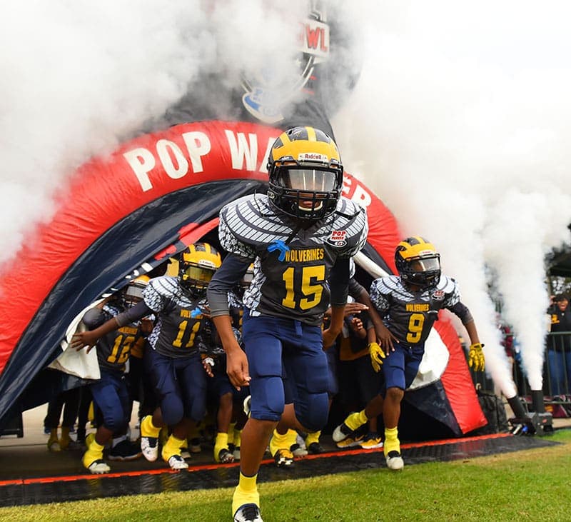 Pop Warner football players running onto the field through the Pop Warner tunnel